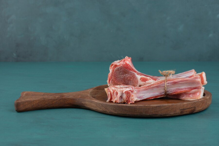 Assorted beef bones including marrow, knuckle, and oxtail on a wooden cutting board with fresh herbs and spices.