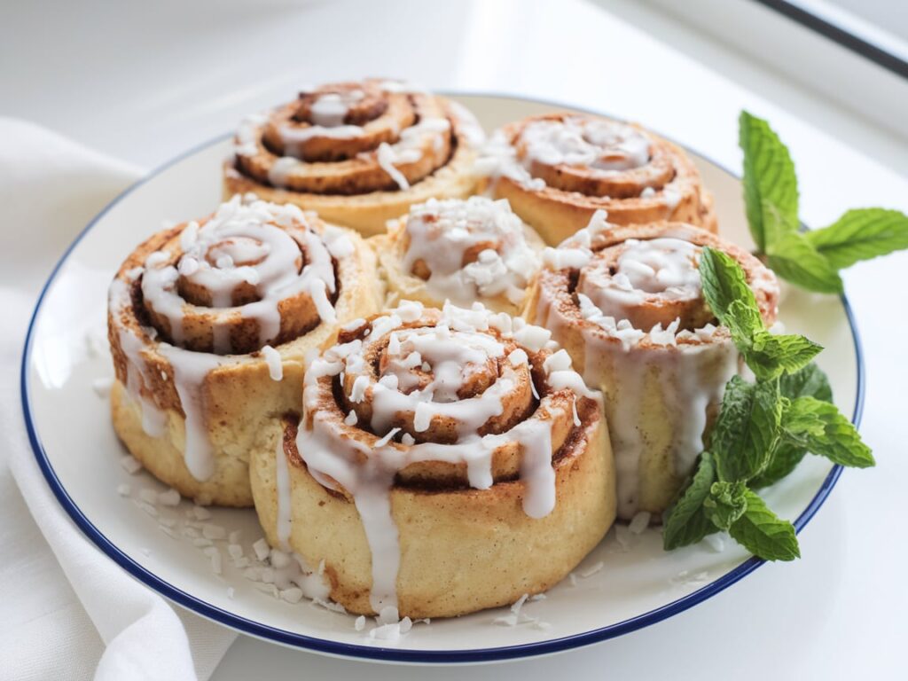 Soft vegan cinnamon rolls topped with coconut cream glaze and sprinkled with shredded coconut.