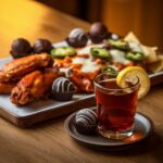 A black tea shot paired with spicy chicken wings, nachos, and chocolate truffles on a wooden table.