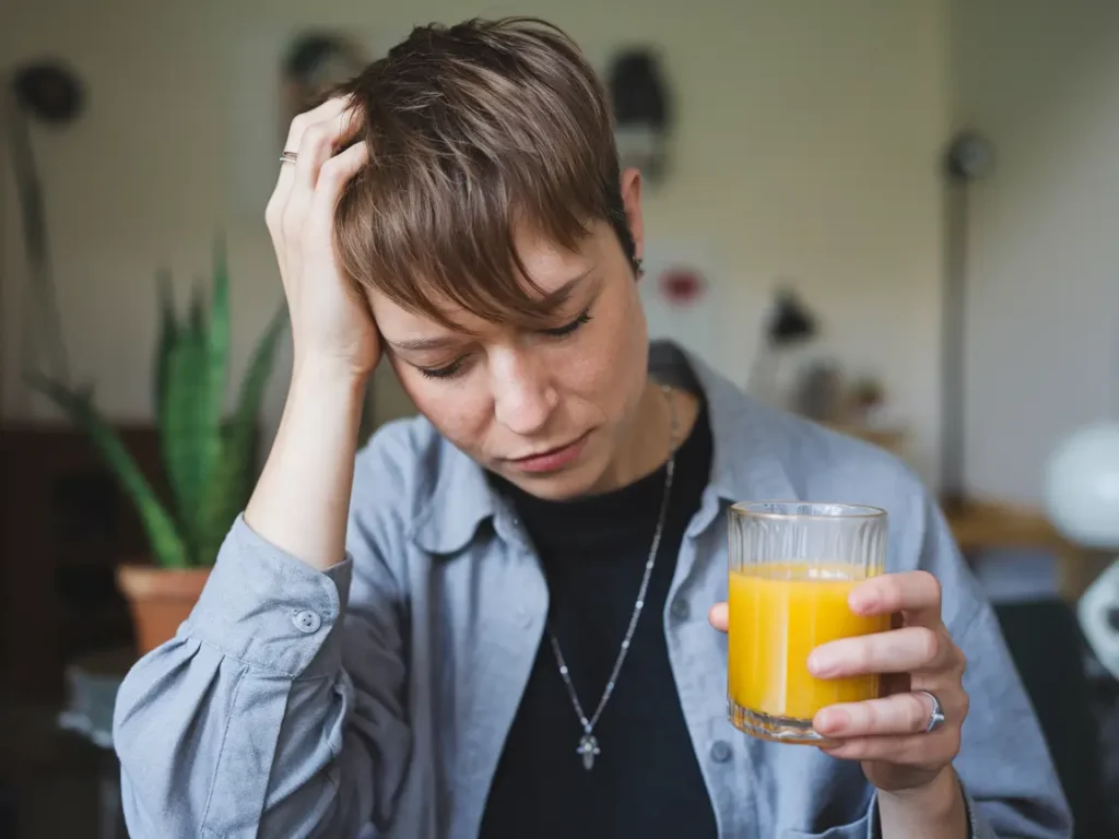 A person experiencing fatigue while holding a glass of juice, representing the struggles of a juice fast.