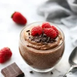 High protein chocolate chia seed pudding topped with berries in a glass bowl.