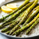 Oven roasted asparagus topped with Parmesan cheese on a serving plate.