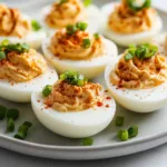 Spicy chili garlic deviled eggs garnished with chili flakes and herbs.