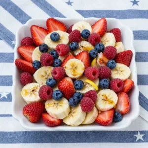 A vibrant red, white, and blue fruit salad in a clear bowl, featuring strawberries, blueberries, and banana slices, perfect for patriotic celebrations.