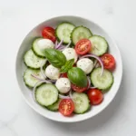 Close-up of a vibrant cucumber Caprese salad with cherry tomatoes, fresh mozzarella balls, and basil leaves, drizzled with balsamic glaze.
