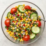 A vibrant bowl of fresh corn salad with cherry tomatoes, red onion, bell peppers, and cilantro, dressed with lime vinaigrette.