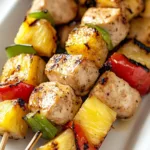 Grilled pineapple chicken kabobs on skewers with vegetables and pineapple chunks.