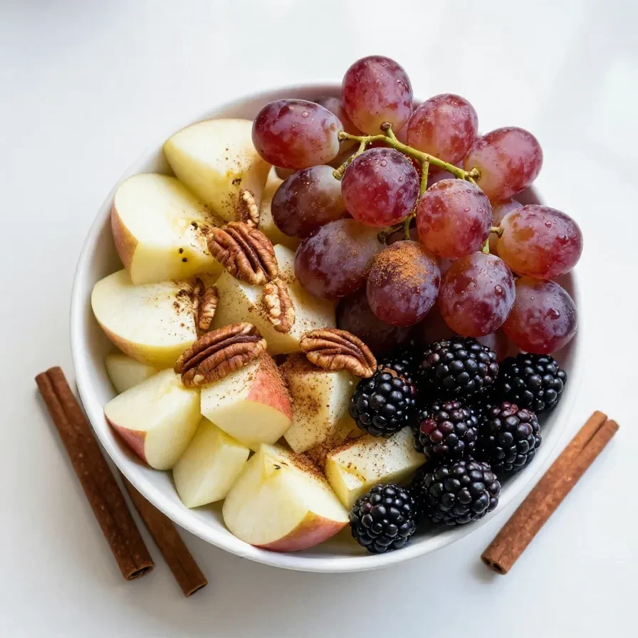 A vibrant bowl of fall fruit salad featuring apples, pears, cranberries, and nuts.