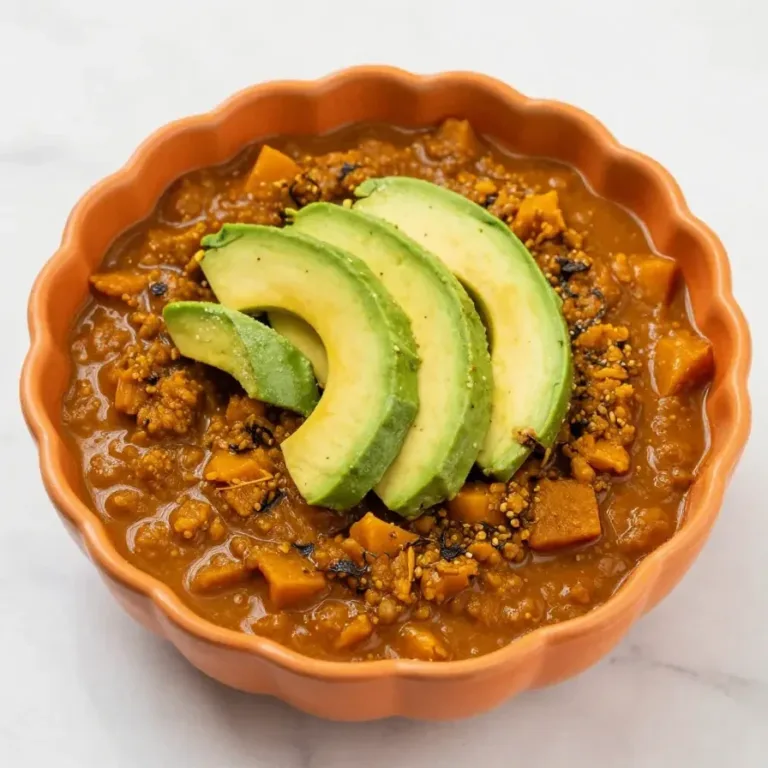 A bowl of vegetarian pumpkin chili garnished with fresh cilantro and served with a side of cornbread.